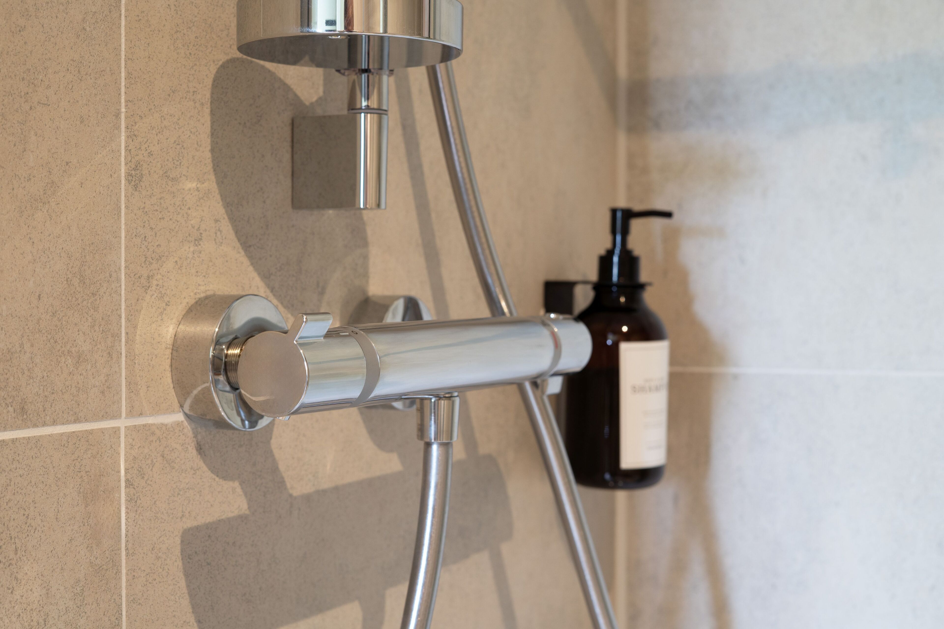 A shower with a chrome hose and wall-mounted controls.