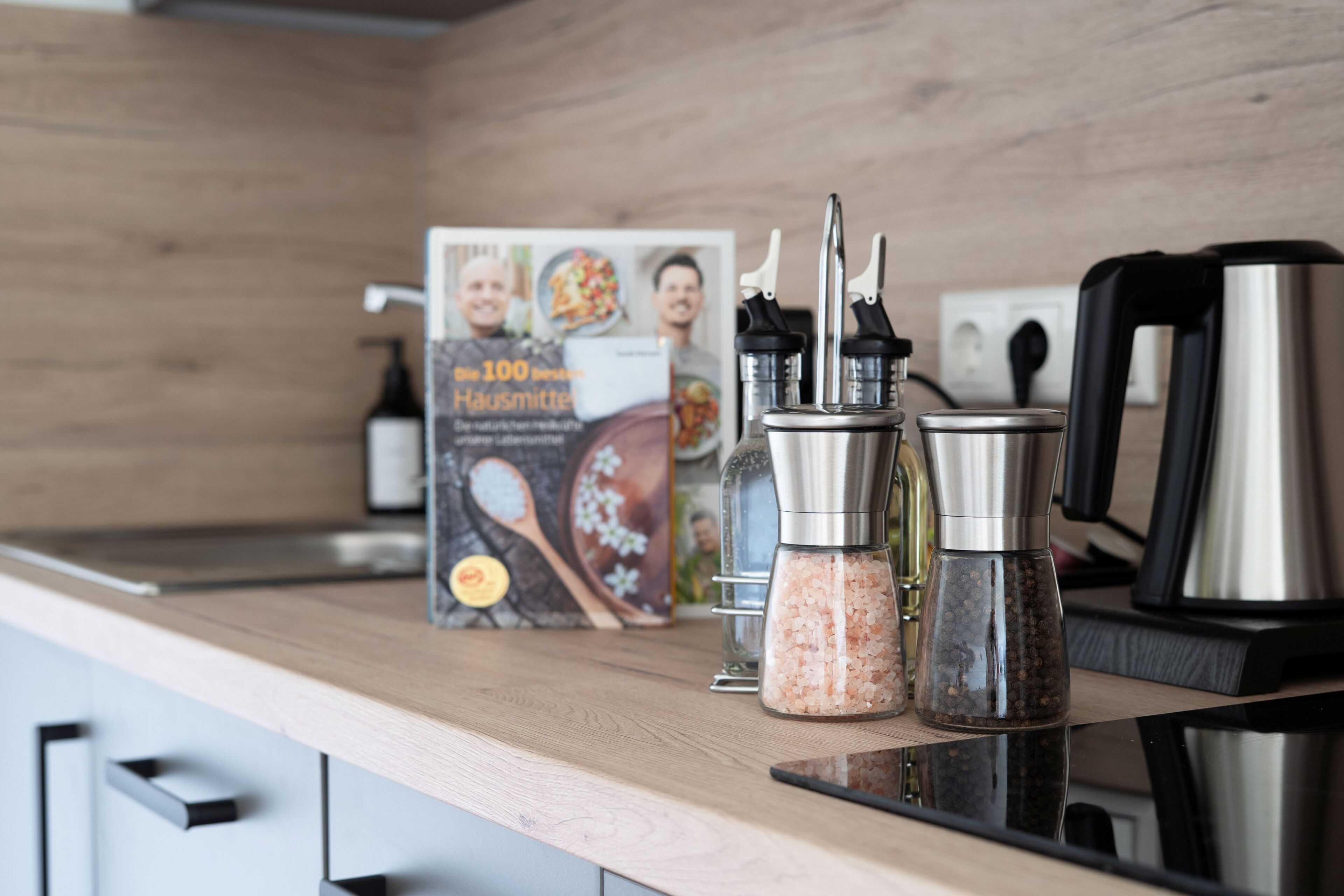 A kitchen counter with a cookbook, salt and pepper shakers, a coffee maker, and a kettle.