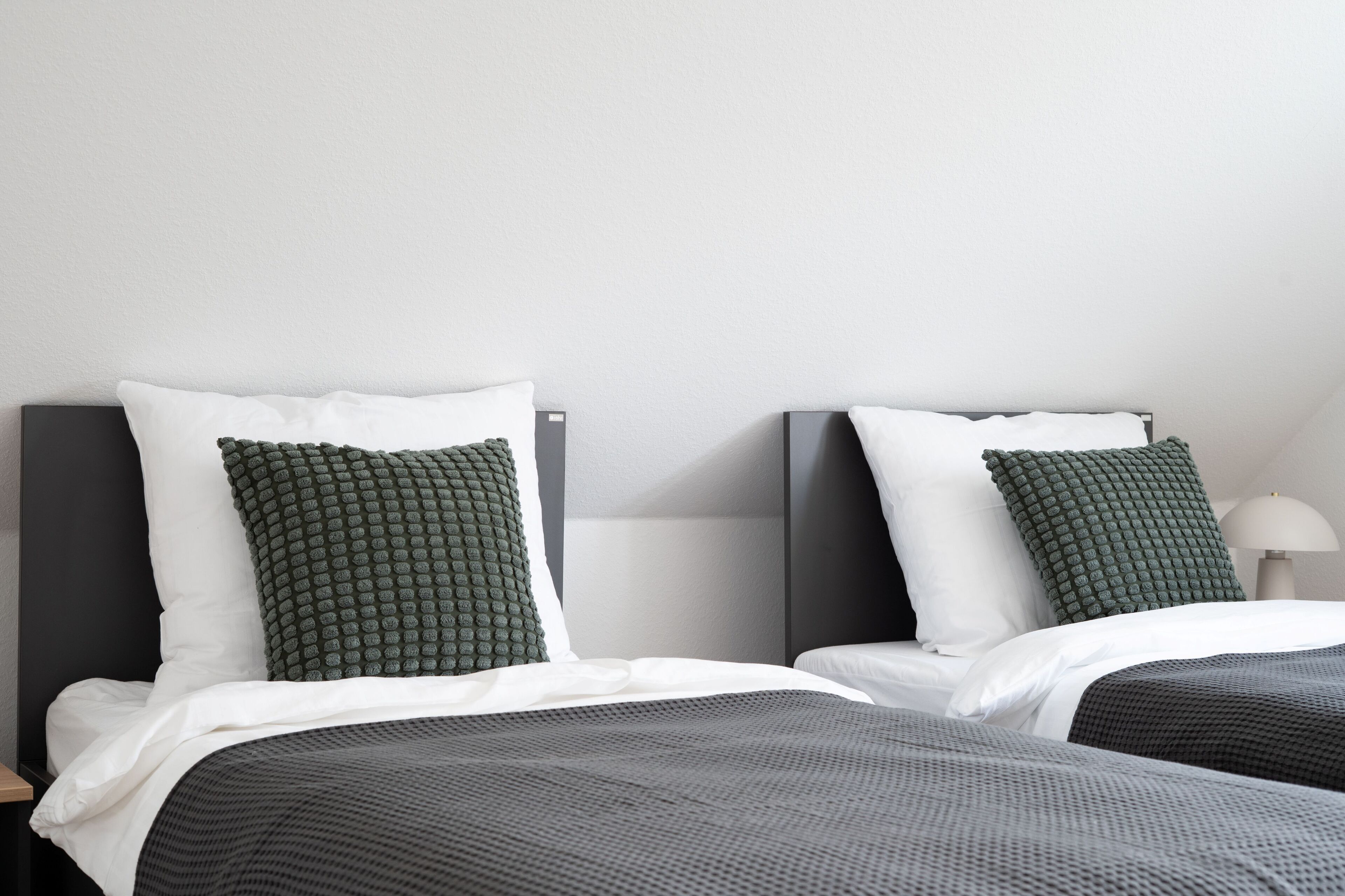 A hotel room with two beds, each with a white pillow and a textured green pillow.