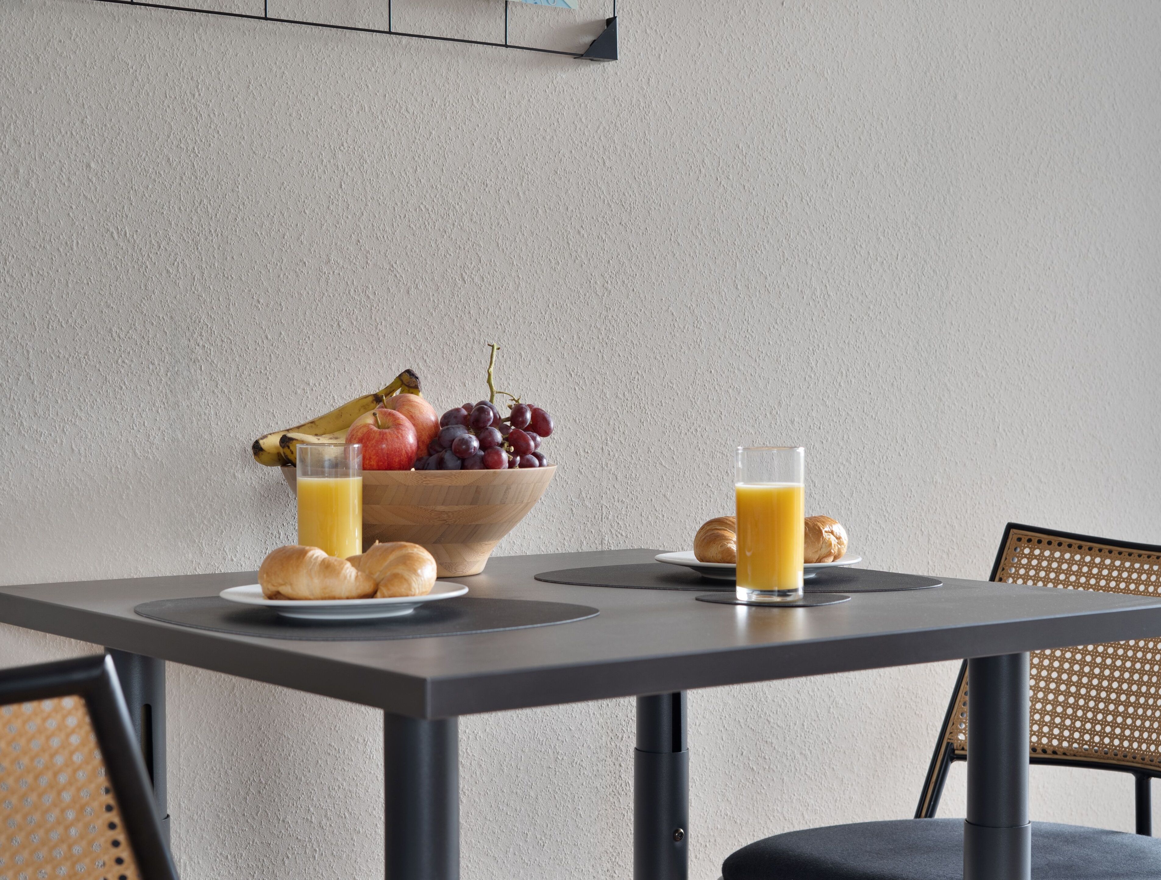 Un desayuno con frutero, croissants y jugo de naranja sobre una mesa.