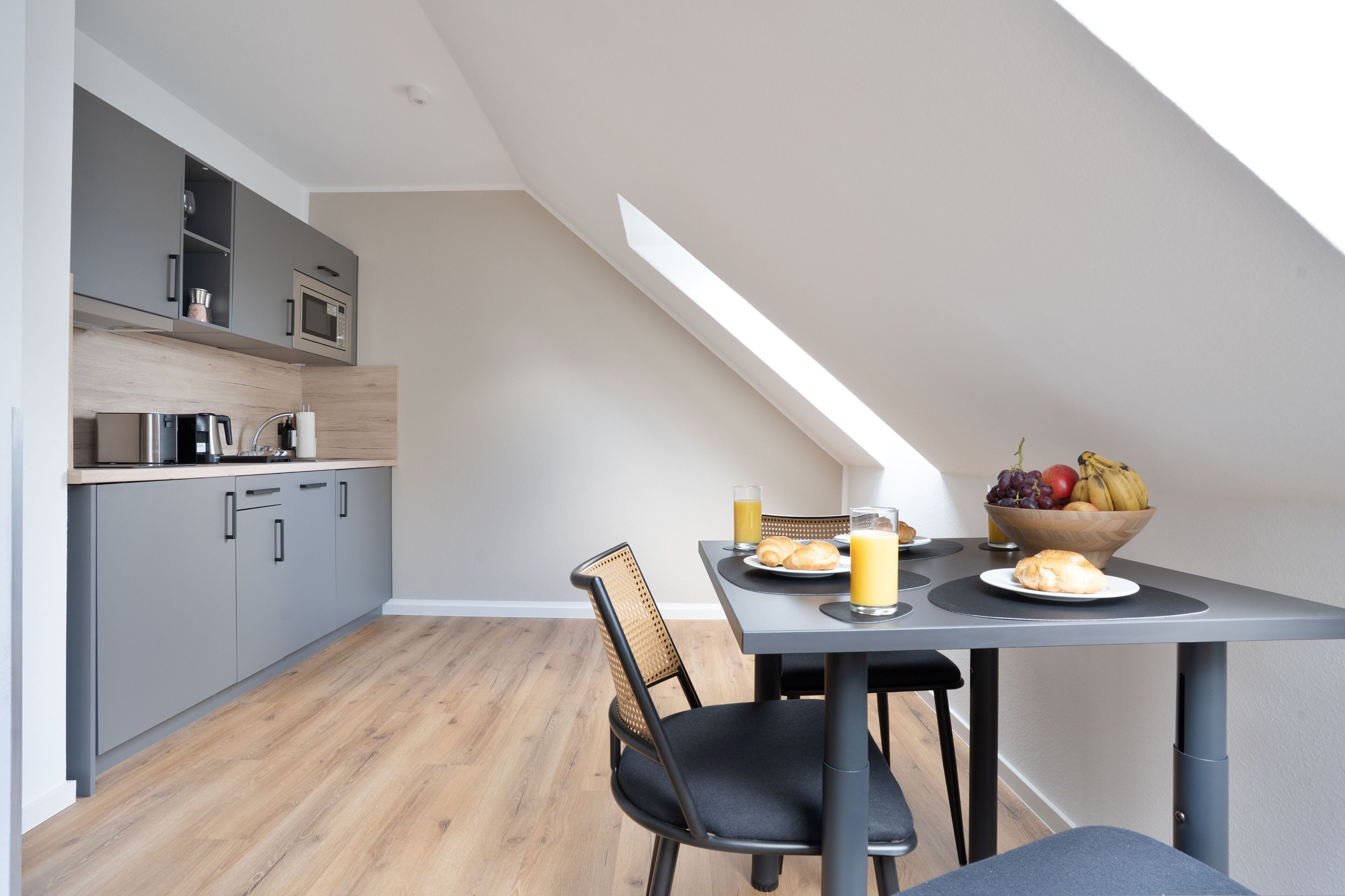 Une cuisine moderne avec des meubles gris, un four à micro-ondes et un coin repas avec une table mise pour le petit-déjeuner.