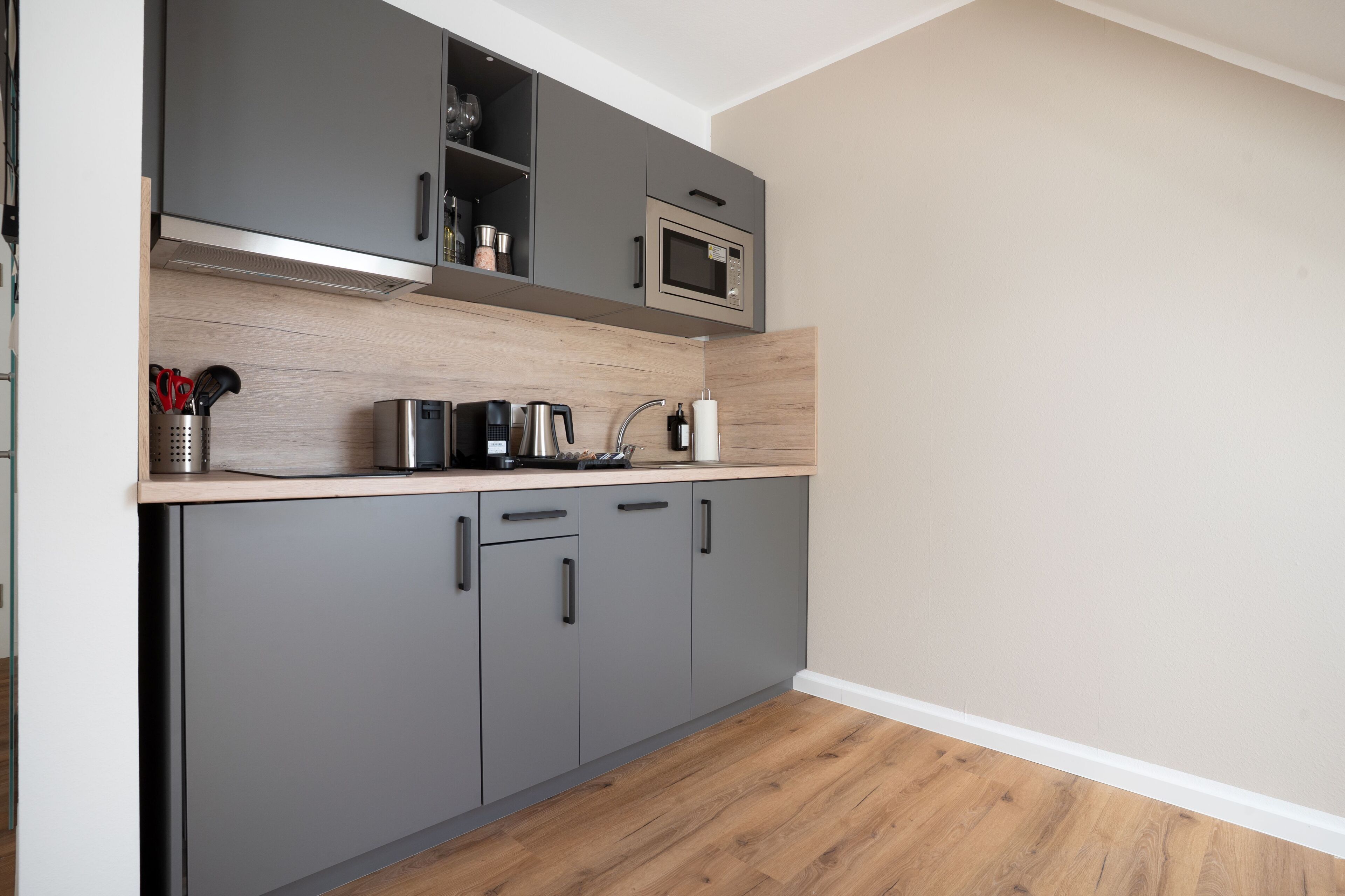 A modern kitchen with grey cabinets, a microwave, a coffee maker, and a kettle.