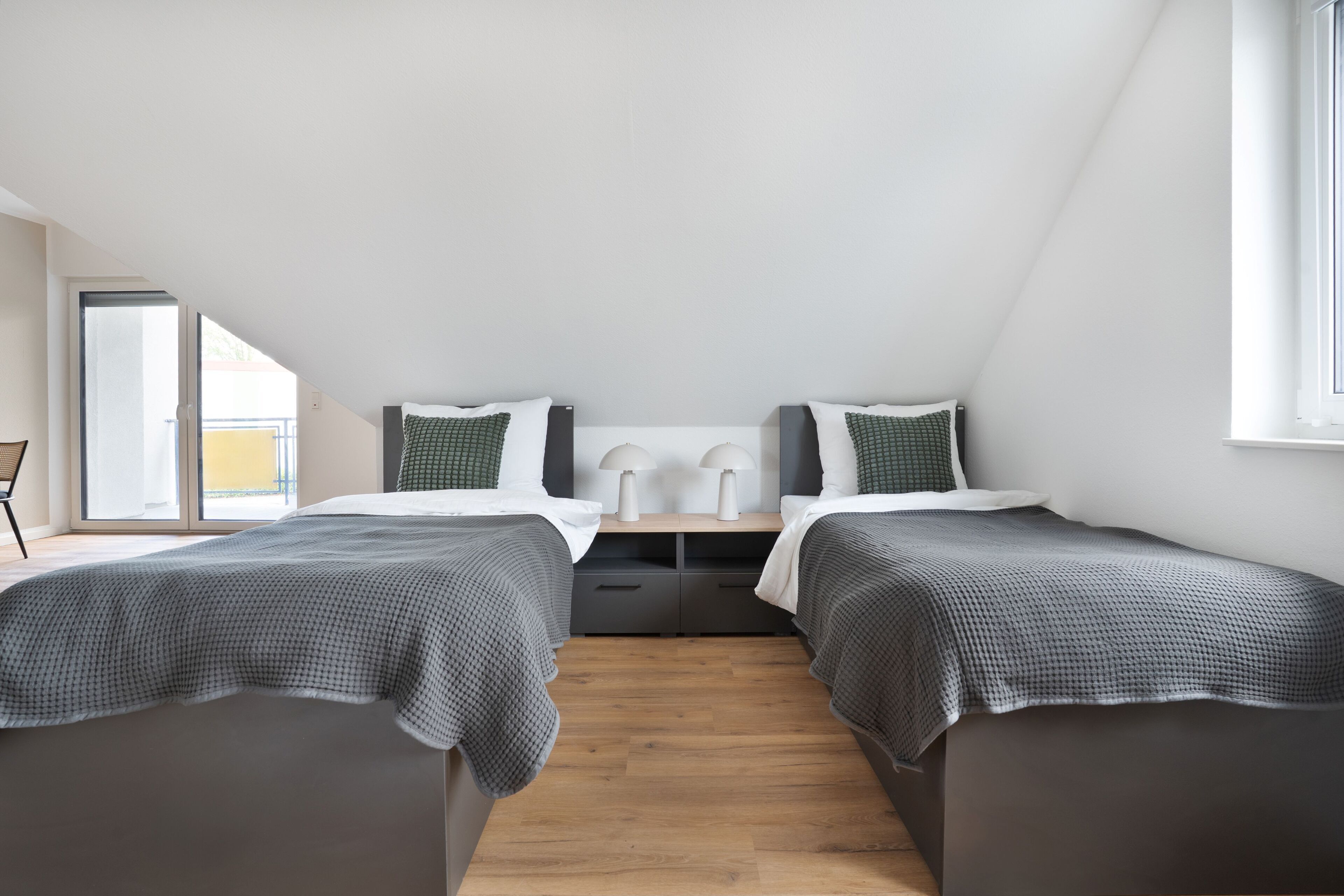 Un dormitorio moderno con dos camas, una mesita de noche y una ventana.