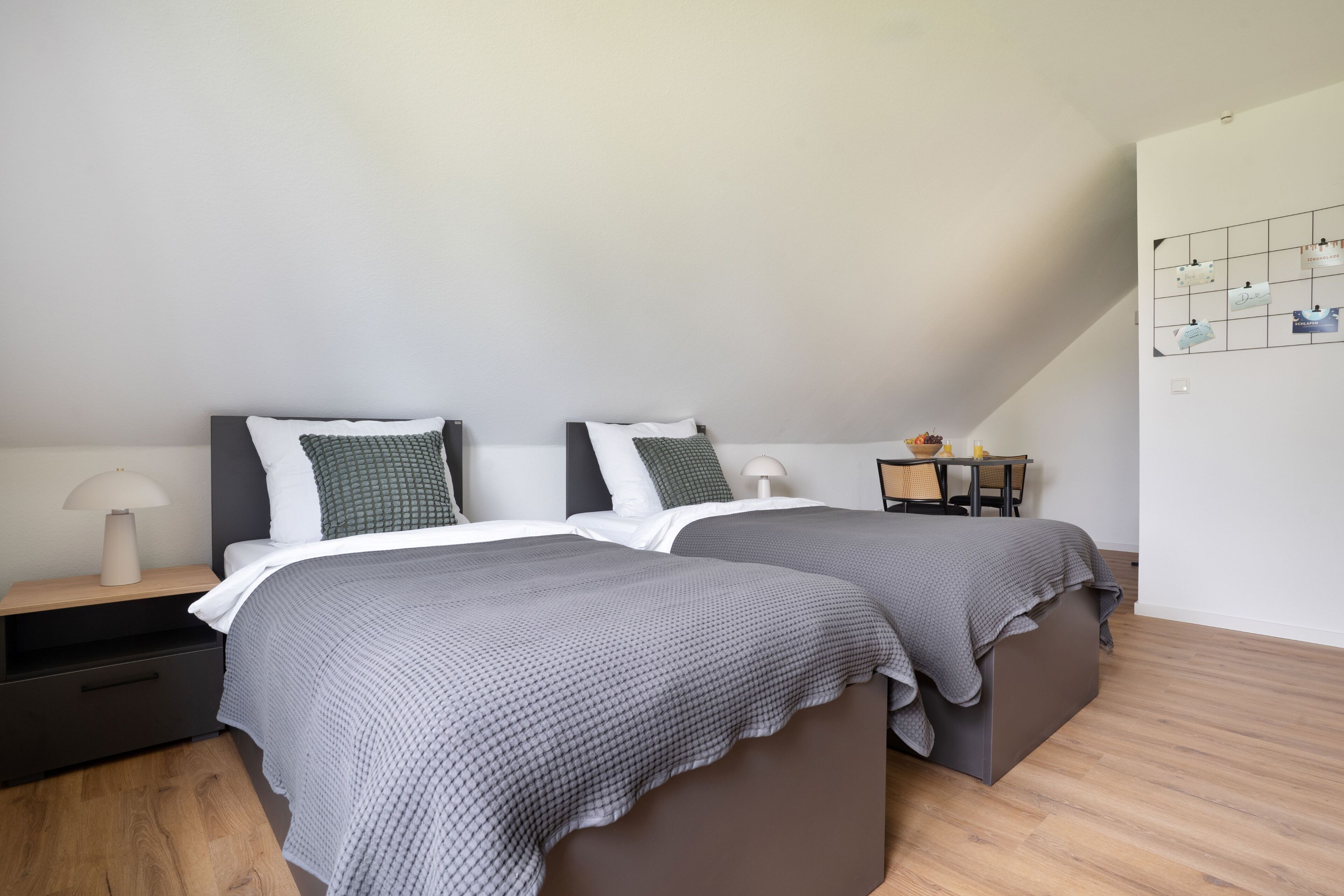 Une chambre avec deux lits, une table de chevet, une lampe et une petite table avec une chaise.