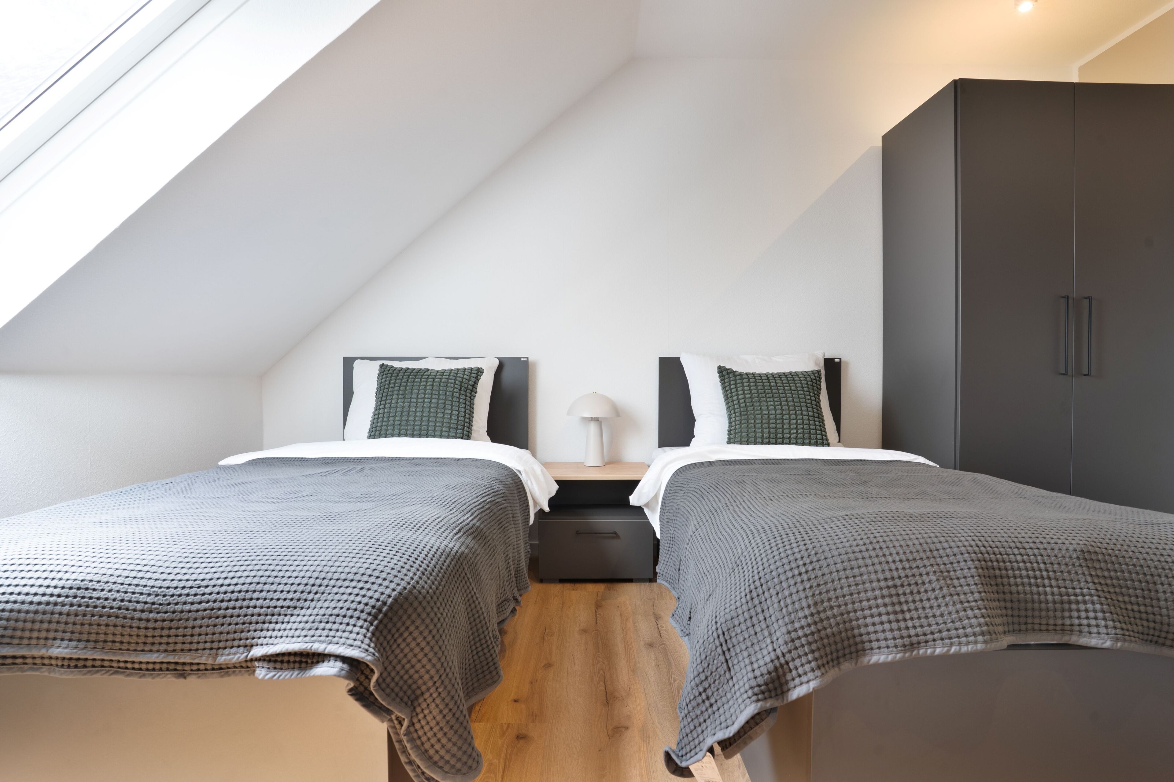 Quarto com duas camas, um guarda-roupa e um claraboia.