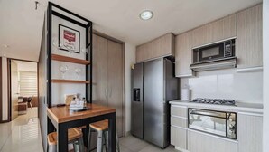 A modern kitchen with a stainless steel refrigerator, a built-in microwave, and a gas stove. There is a wooden dining table with two stools. - EP| Modern 2BR W/Workspace, Fast Internet, SmartTv (Medellín)