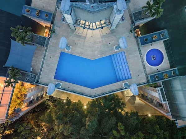 Vista aérea de un hotel moderno con una piscina rectangular grande, zona de estar exterior y una fuente circular.