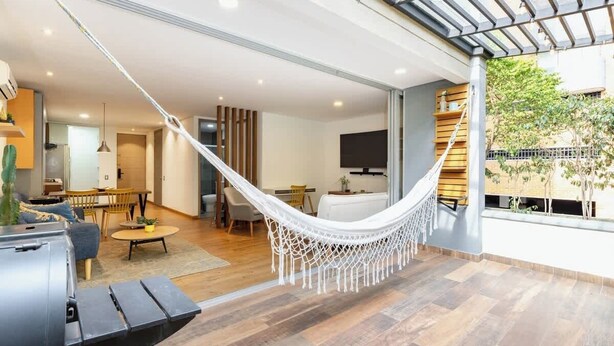 A modern living room with a hammock, wooden flooring, and a large window overlooking a garden. - |EP| Bright Apt w/Terrace, AC, BBQ and Workspace (Medellín)