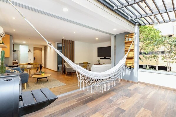 A modern living room with a hammock, wooden flooring, and a large window overlooking a garden.