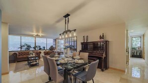 A spacious living room with a large window, a dining area with a glass table, and a grand piano. - EP|  3 bed/ Br Apt W/city views, Great Location (Medellín)