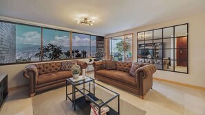 A living room with a large window, a sofa, a coffee table, and a kitchen area visible through the window. - EP|  3 bed/ Br Apt W/city views, Great Location (Medellín)