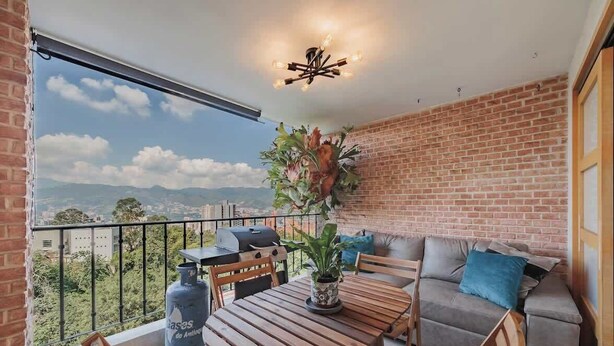 A balcony with a wooden table and chairs, a sofa, and a potted plant. - EP|  3 bed/ Br Apt W/city views, Great Location (Medellín)