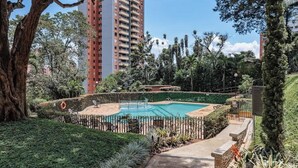 A swimming pool surrounded by a fence, with a tall building in the background.