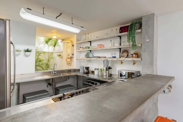 A modern kitchen with stainless steel appliances, white cabinetry, and a concrete countertop.