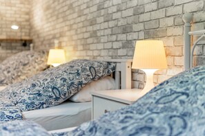 A bedroom with a brick wall, two bedside tables with lamps, and patterned bedding.