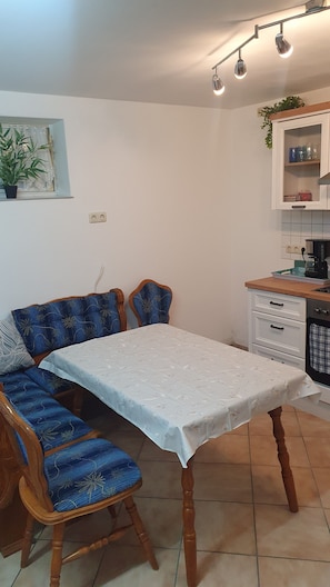 Et spiseområde med et bord, stole, et køkken og en potteplante.