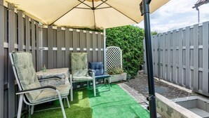A patio area with a table and two chairs, a green artificial turf, and a wooden fence.
