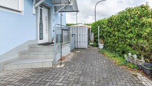 A paved pathway leading to a building with a red roof, a white door, and a small set of steps.