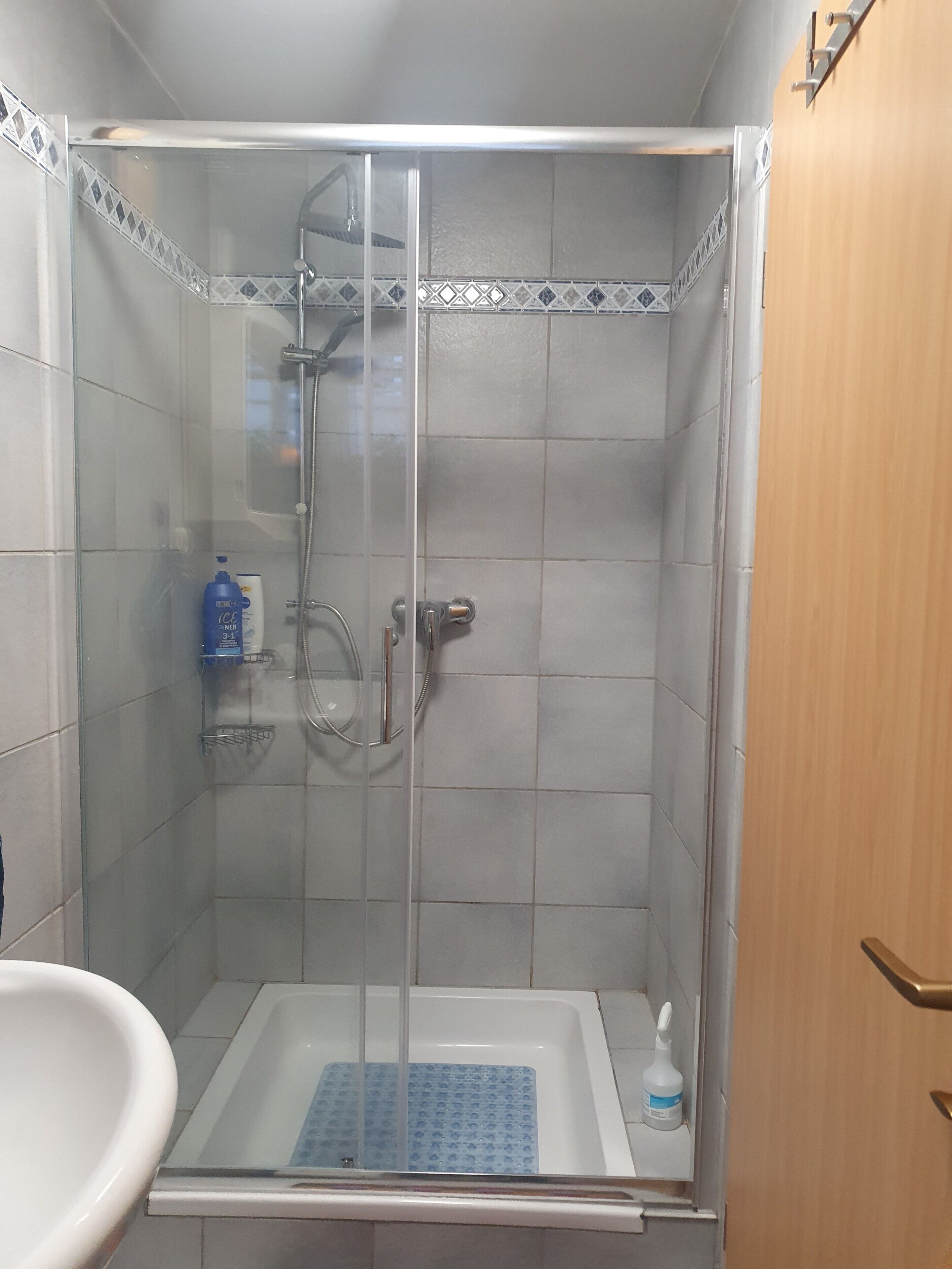 Una cabina de ducha con puerta de cristal, una bañera blanca y un estante pequeño con artículos de aseo.