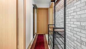 A narrow hallway with a wooden door, a red carpet, and a metal rack against a brick wall.
