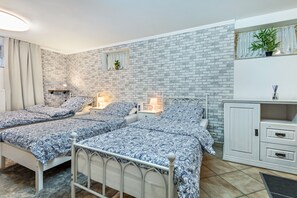 Ein Schlafzimmer mit zwei Betten, einem weißen Kleiderschrank, einem kleinen Fenster mit Vorhängen und einer Backsteinwand.