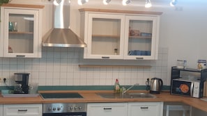 Et køkken med hvide skabe, emhætte i rustfrit stål, indbygget ovn, kaffemaskine og mikrobølgeovn.