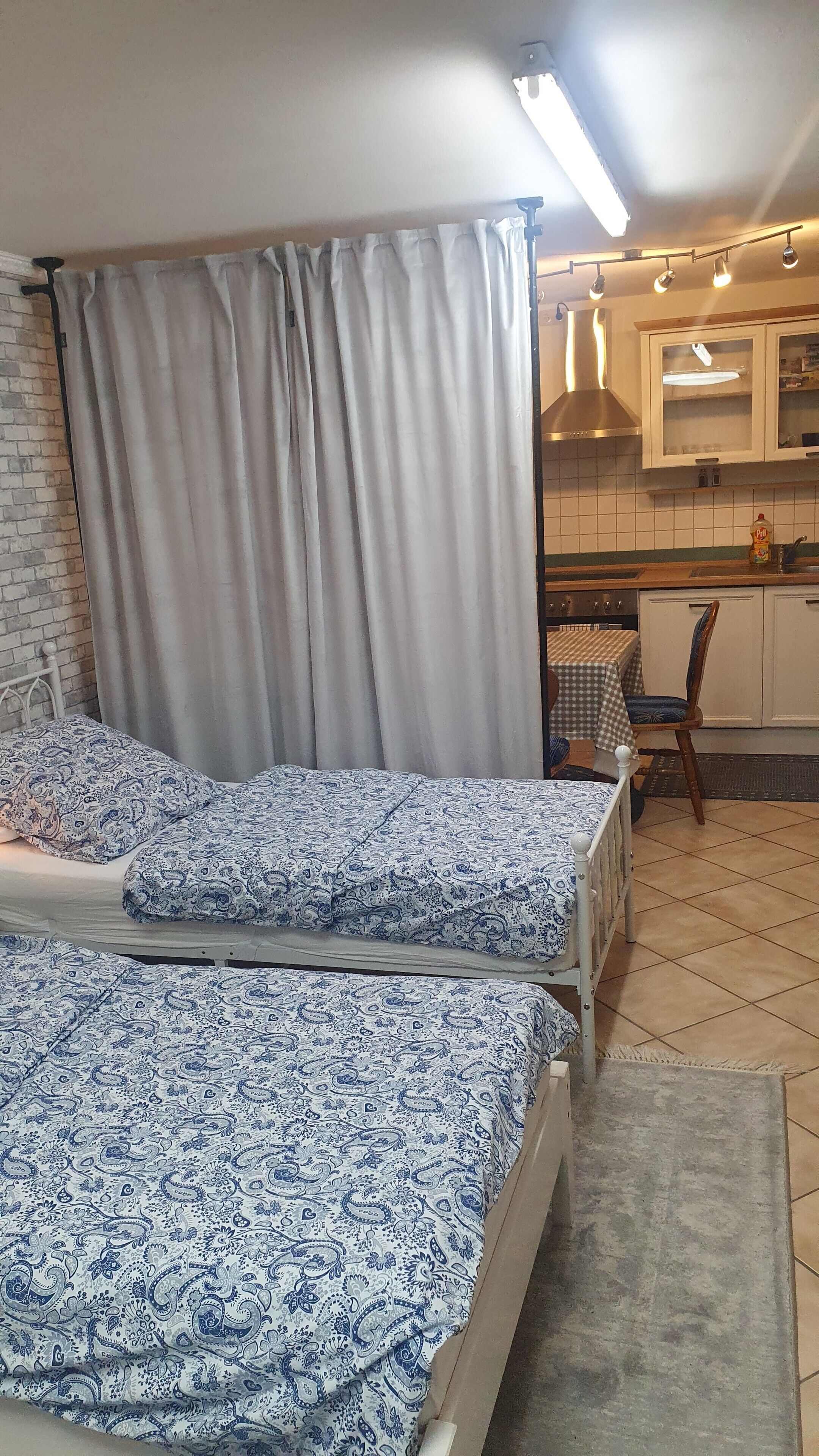 Une chambre avec deux lits, une fenêtre avec des rideaux, un coin cuisine et un espace repas.