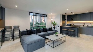 A modern apartment with a grey sofa, a glass coffee table, and a kitchen area with bar stools. - |EP| Spacious Apt with AC, Workspace, Views (Medellín)