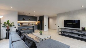 A modern living space with a kitchen, a grey sofa, a coffee table, and a flat-screen TV mounted on the wall. - |EP| Spacious Apt with AC, Workspace, Views (Medellín)