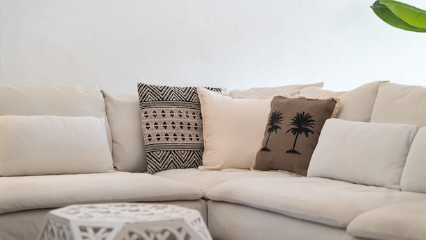 A beige sofa with patterned and palm tree pillows, a white side table, and a plain wall. - Retiro T2 c/Piscina em Porches por Lovelystay (Alporchinhos)