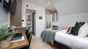 A modern bedroom with a bed, bedside table, and a desk with a computer and notebook. - Camden | Room B3 - Studio Apartment, Sleeps 2 (London)