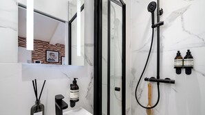 A modern bathroom with a white sink, black fixtures, a glass shower enclosure, and marble walls. - Camden | Room B3 - Studio Apartment, Sleeps 2 (London)
