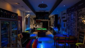 Un espace bar équipé d’une table de billard, de tabourets et d’un panneau lumineux au néon.
