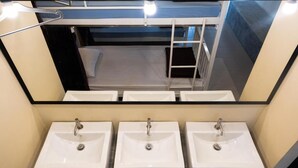 Une salle de bain avec trois lavabos blancs et un grand miroir au-dessus.