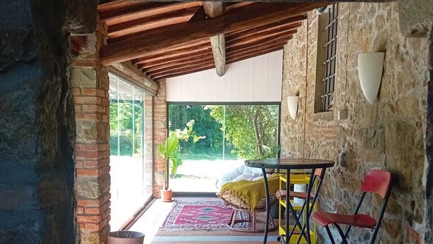 A rustic patio with a wooden table and chairs, a stone wall, and a view of greenery outside. - Suite in Tuscan farmhouse between Florence and Arezzo with wifi and pool (Pian di Scò)