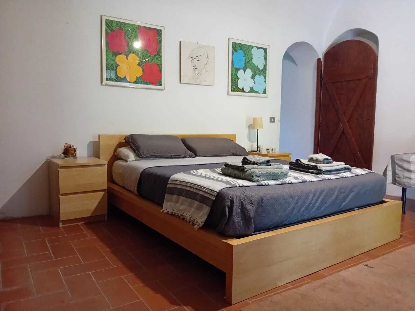 A bedroom with a wooden bed, a nightstand, a lamp, and artwork on the wall.