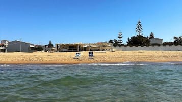 Una playa con aguas cristalinas, una orilla de arena y un edificio con zona techada.