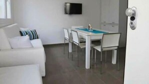Un espacio habitable compacto con zona de comedor, sofá, televisor montado en la pared y puerta con cerradura.