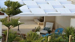 Un área de estar moderna al aire libre, con sombrillas blancas, sillones de descanso y diversas plantas.