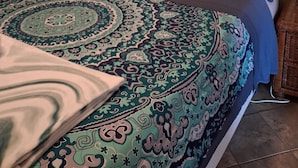 Une chambre à coucher comprenant un lit, une tête de lit, un panneau décoratif fixé au mur, une table de chevet, une lampe et une couverture à motifs.