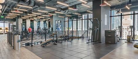 Un gimnasio moderno con equipamiento de ejercicio, ventanas amplias y un techo alto con vigas a la vista.