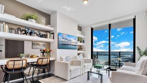 Un salon moderne avec un coin repas, de grandes fenêtres offrant une vue sur la ville et une bibliothèque.