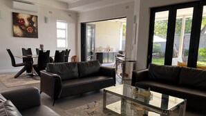 Ein modernes Wohnzimmer mit zwei schwarzen Ledersofas, einem Glastisch und einem Essbereich mit einem Tisch und Stühlen.
