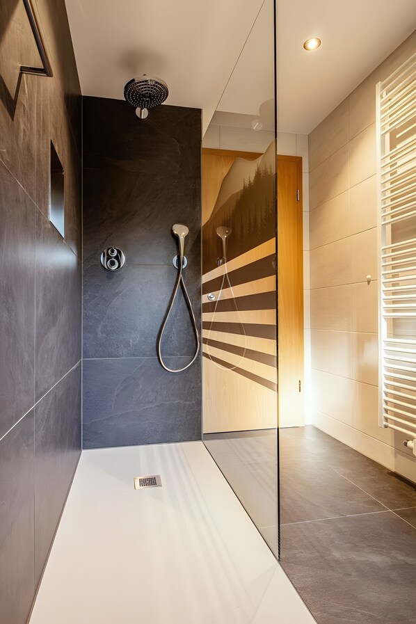 Une douche moderne dotée d’un pommeau de douche à main, d’un panneau de commande mural et d’une paroi en verre.