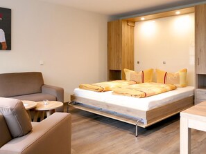 Un dormitorio moderno con cama, sofá, una pequeña mesa redonda y armarios empotrados de madera.