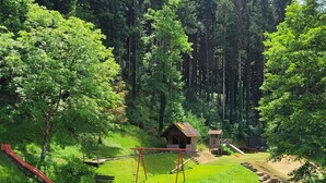 Un parque infantil con columpios, un tobogán y una pequeña estructura de madera en un área boscosa.