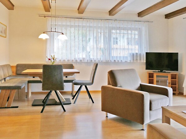 A modern living room with a sofa, chairs, a dining table, and a TV.