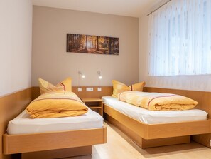 A hotel room with two beds, a painting on the wall, and a window with curtains.