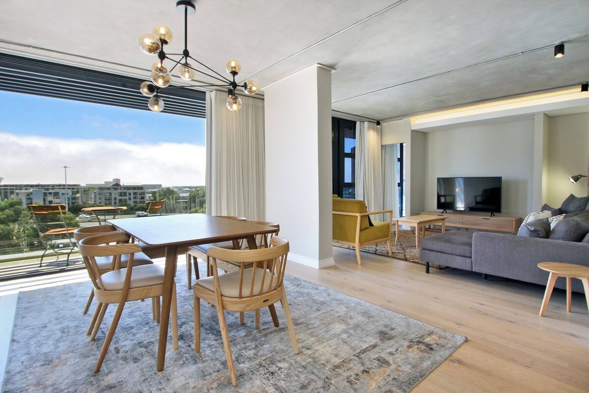 A modern living room with a dining area, a sofa, a TV, and a city view.