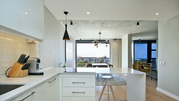 A modern kitchen with white cabinetry, a central island, and a view of the city through large windows.